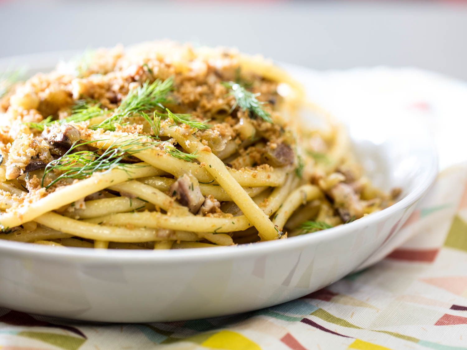 A shallow white bowl filled with a mound of pasta con sarde topped with bread crumbs