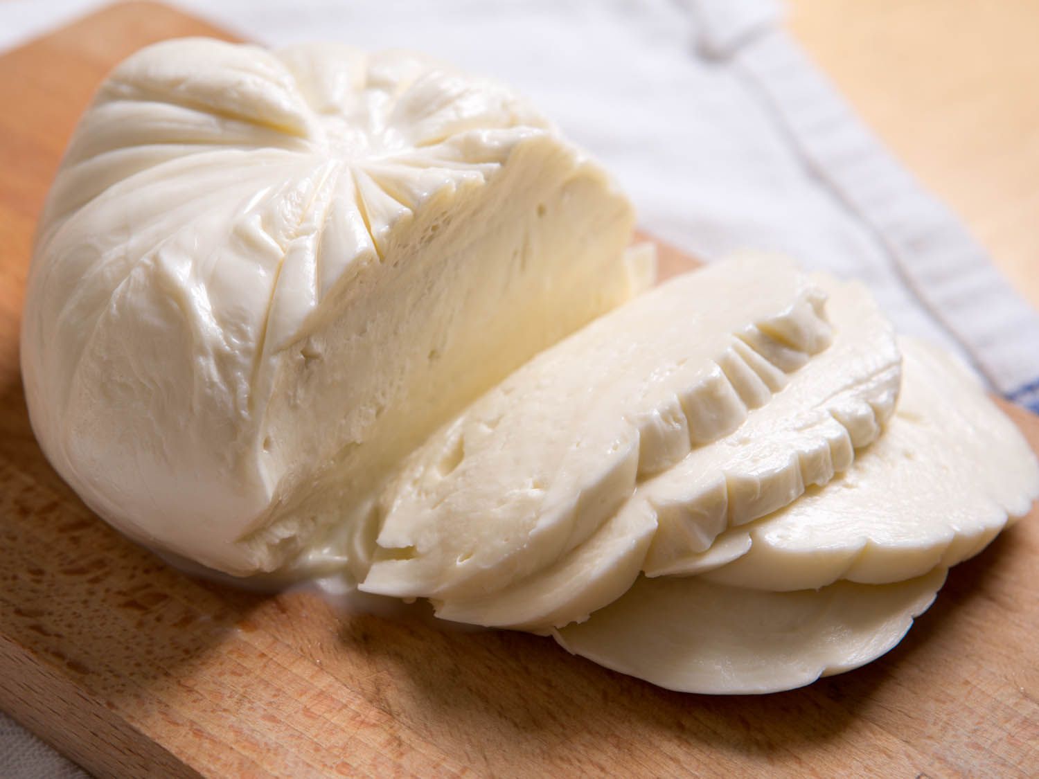 一团新鲜的马苏里拉奶酪放在砧板上。已经切了四片奶酪放在板上。