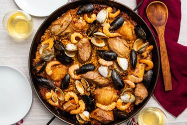 A pan of grilled paella mixta on a table, with mussels, shrimp, chicken, and clams.
