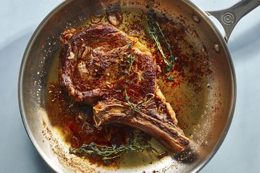 A seared bone-in rib eye with aromatics in a stainless steel skillet.