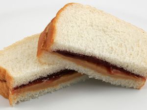 在白色的切片面包,花生酱和果冻三明治切成两半的削减双方面临的相机。