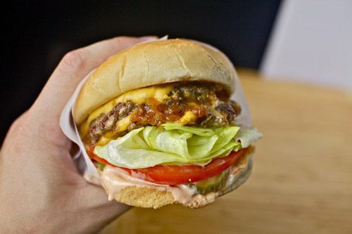 A finished homemade Animal Style Double-Double In-N-Out burger held by a hand.