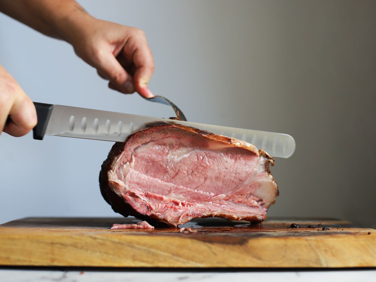 一只手正在用切片刀切下一块放在木砧板上的上等烤肋排