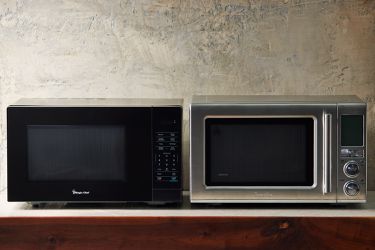 two microwaves on a wooden countertop