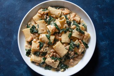 A bowl of paccheri pasta with flavorful sauce of beans and greens.