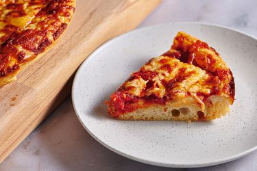 一块新英格兰希腊式披萨放在一个斑点陶瓷盘子上。在图片的左边有一块切披萨的砧板