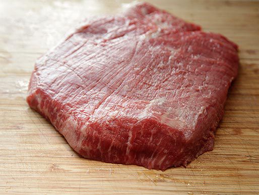 Flank steak on a wooden cutting board.
