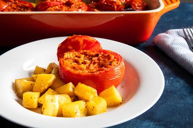 A plate of Roman rice-stuffed tomatoes, served with roasted potatoes in a white bowl.