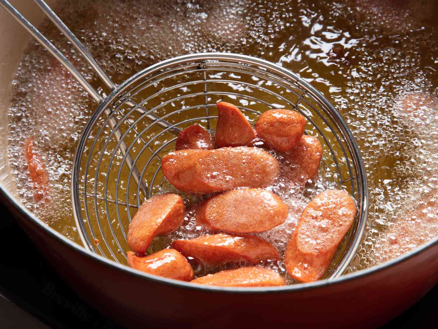 Sliced hotdogs sizzle in a pot of bubbling hot oil.