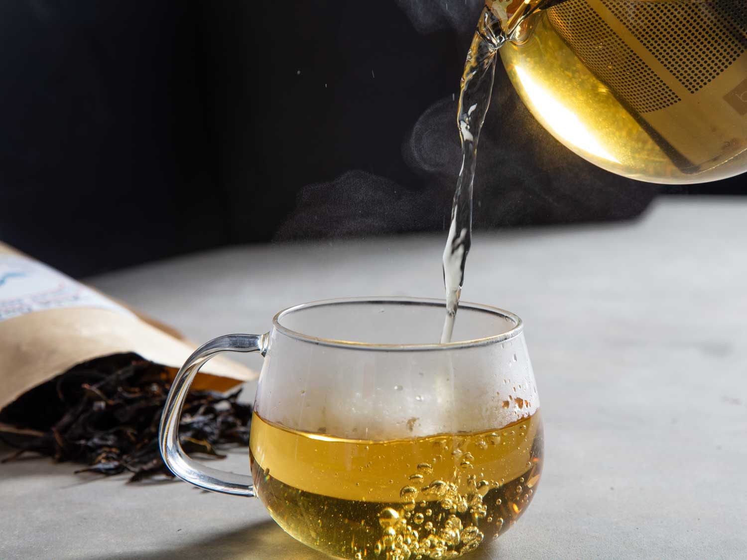 金色的乌龙茶被倒入有柄的玻璃杯中，背景是散叶茶