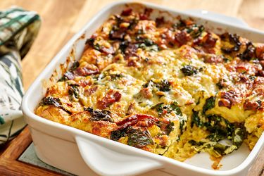 Kale and bacon strata in a baking dish with one portion removed