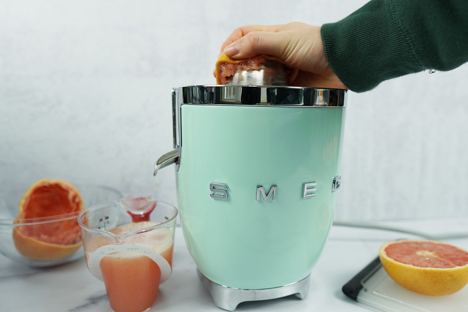 a hand juicing a grapefruit half on the Smeg electric citrus juicer