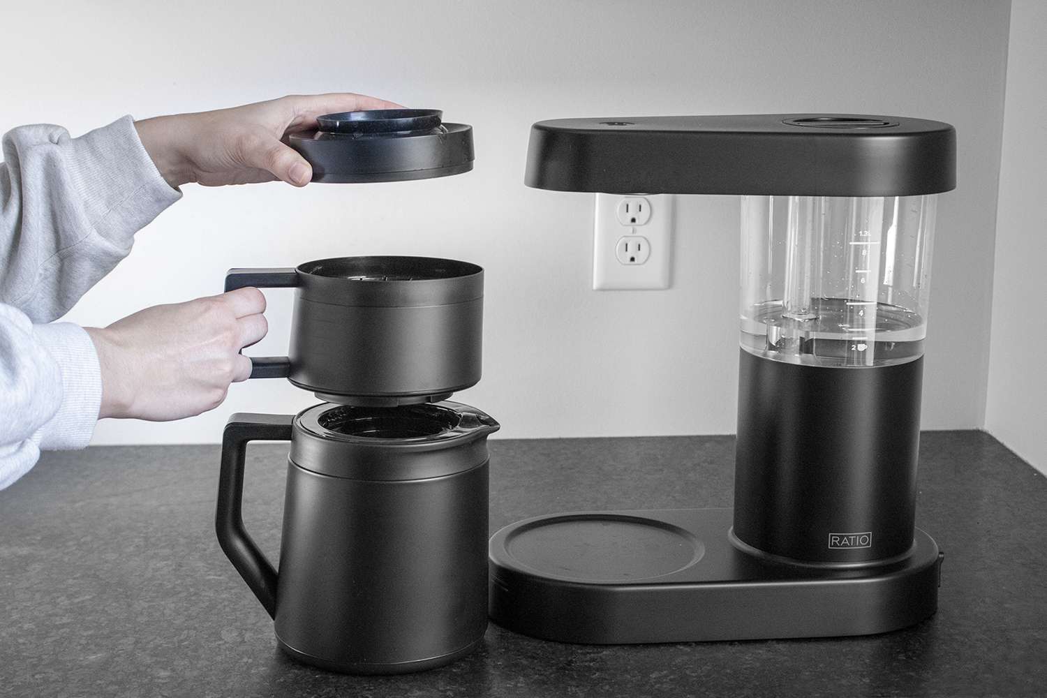 Hands holding the multiple components of the Ratio Six's carafe and brewing system