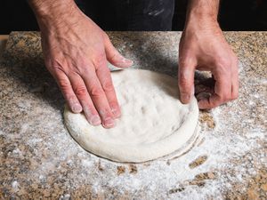 Hands shaping outdoor pizza oven pizza dough on a floured counter
