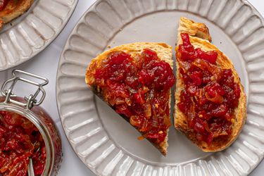 两片面包涂上西红柿和洋葱酱，放在奶油色的脊状陶瓷盘上。在图像的左上角是一个装满果酱的玻璃罐，在左上角是另一个盘子的一部分，上面有更多的吐司。
