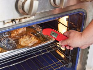 一个人使用一个温度计的温度鸡大腿烤箱里烤