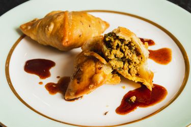 Two kheema samosas on a plate, one broken open to show its interior