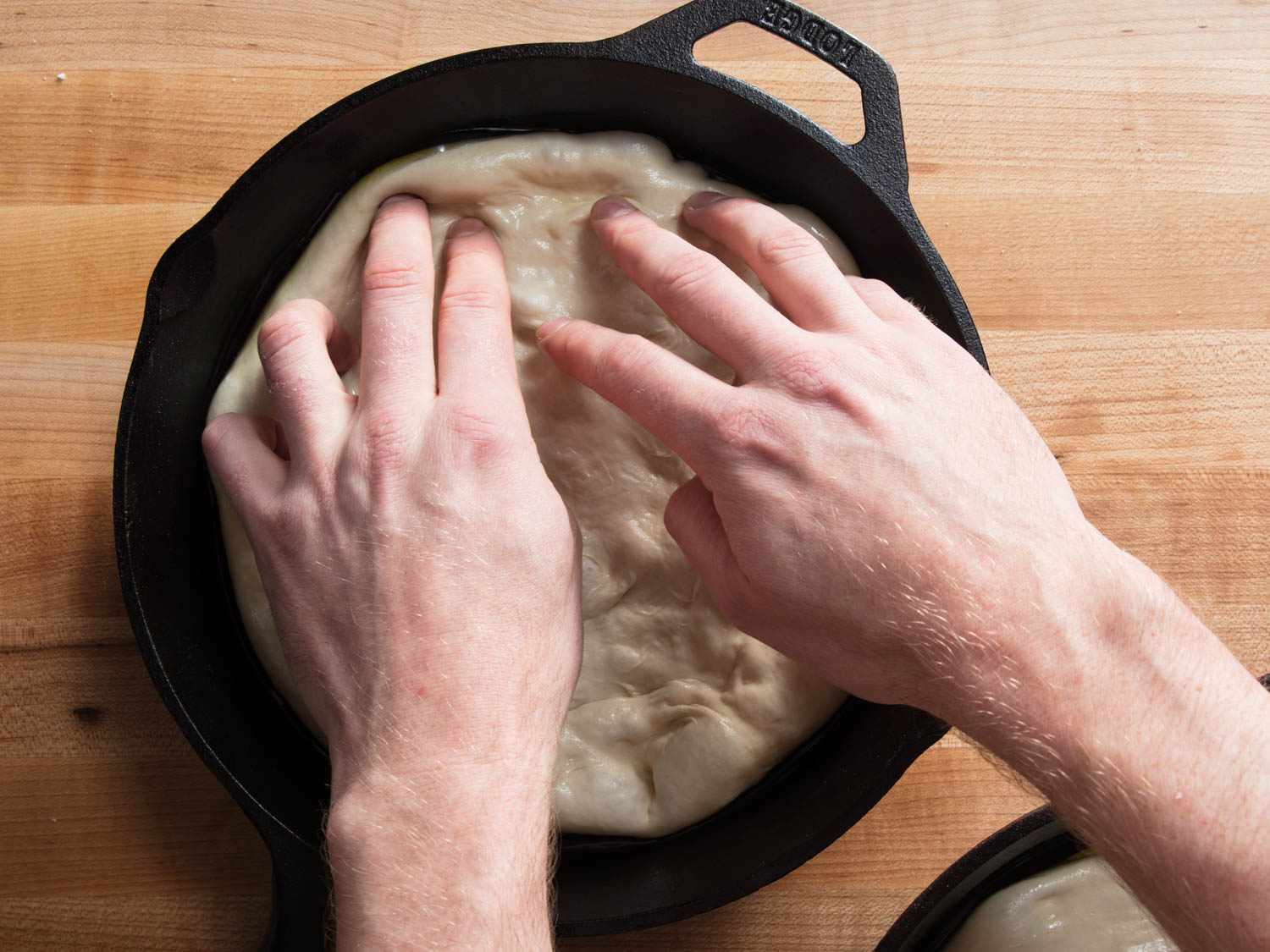 将柔软的披萨面团在铸铁锅中压成圆形。gydF4y2Ba