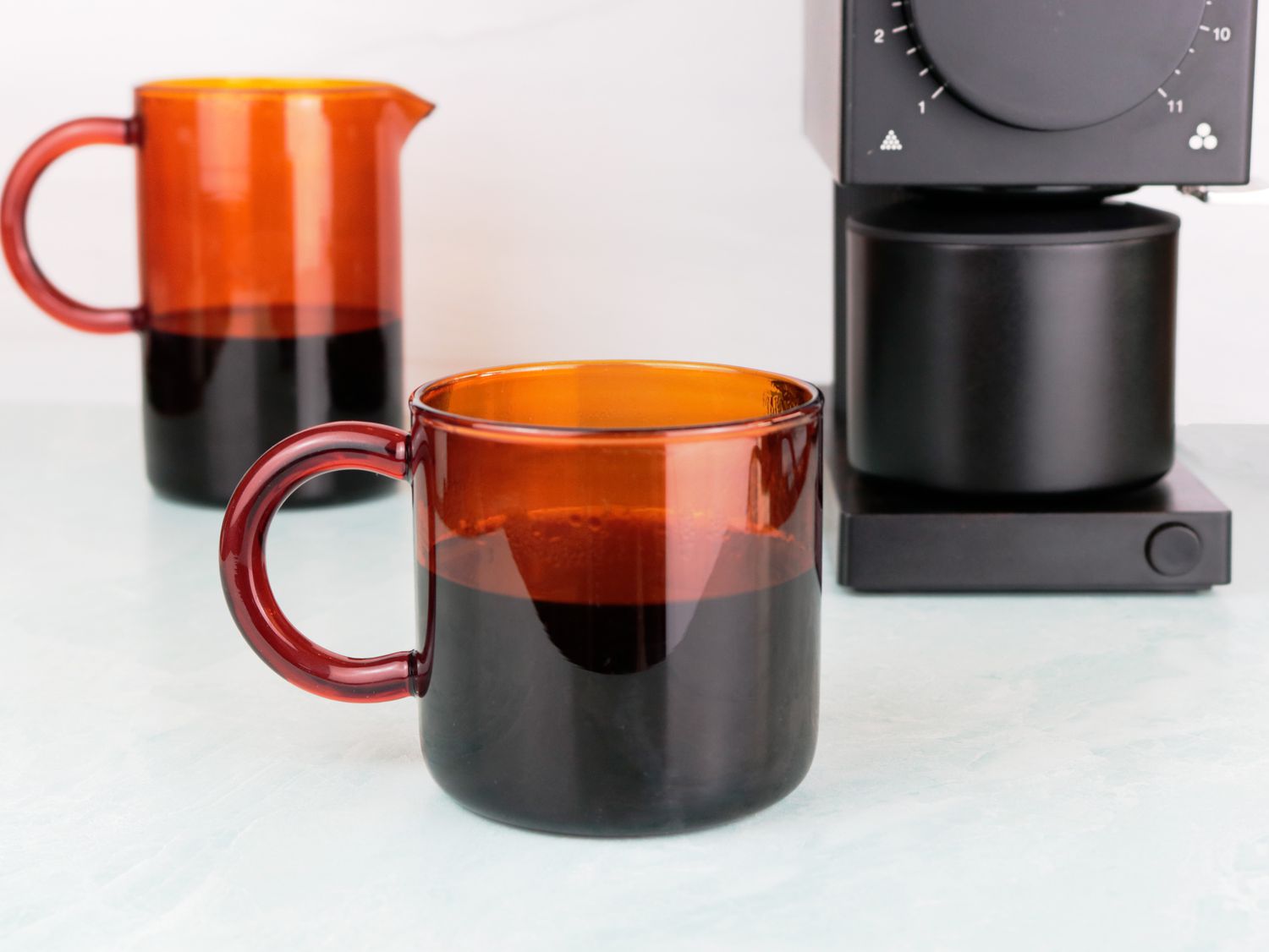 a Manual amber glass coffee mug next to a carafe and coffee grinder