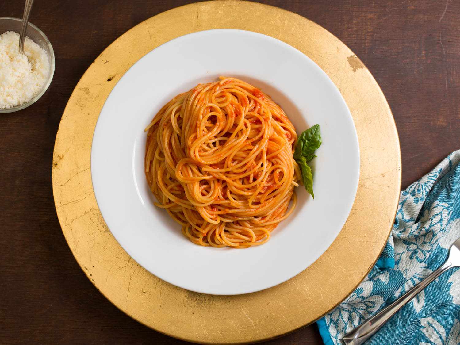 意大利面配番茄酱，装在白色盘子里，放在黄色充电器上。