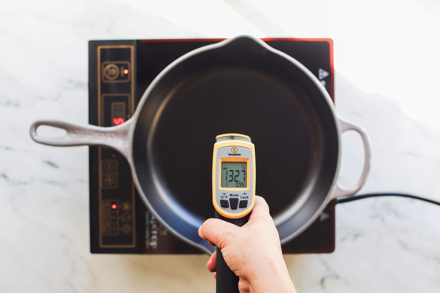 用红外线温度计测量在感应燃烧器上加热的煎锅表面的温度。