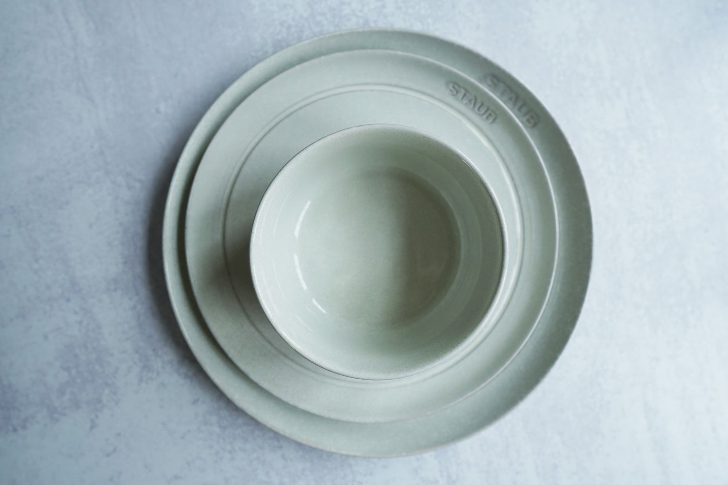 a Staub, white dinnerware place setting on a grey surface