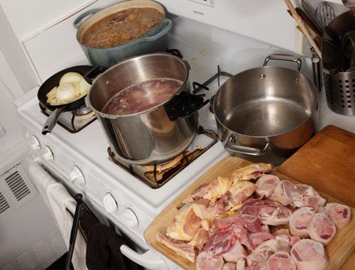 两锅肉汤，一个铸铁煎锅里的洋葱在炉子上煮着，一块切菜板上满是猪肉和鸡肉。