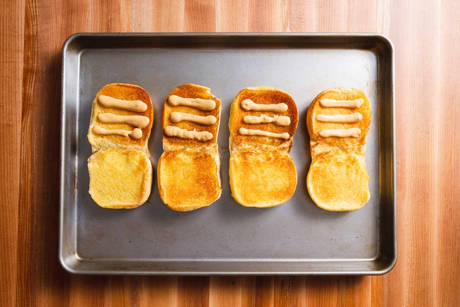 四个烤好的汉堡面包放在烤盘上，每个面包上都有三行自制的Shack酱汁。