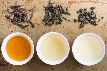 Three white cups of oolong tea next to their respective tea leaves