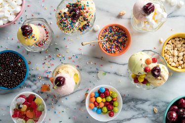 Small dishes of assorted ice creams topped with sprinkles, candies, nuts, and fruit