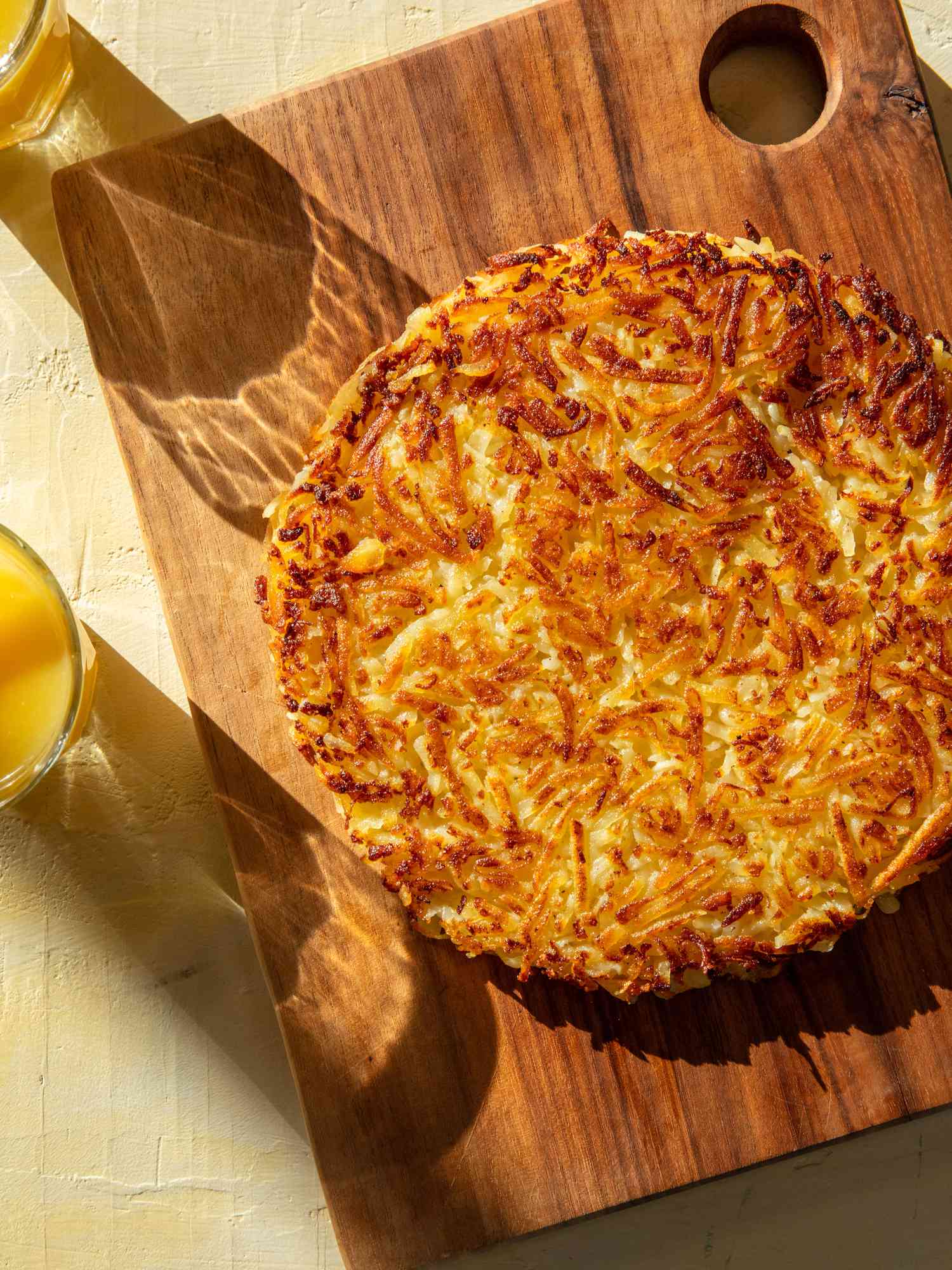 RÃ¶sti on a wooden board with glasses of orange juice nearby.