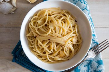 overhead shot of a bowl of pasta aglio e olio, garlic cloves in the background