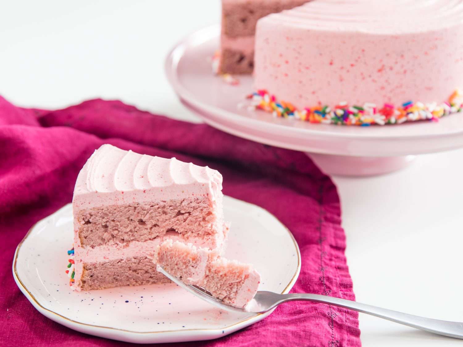 一块双层草莓蛋糕，涂上草莓糖霜，放在蛋糕架上，放在剩下的蛋糕旁边
