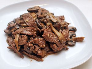 白色的盘子里有一堆炒牛肉和蘑菇。