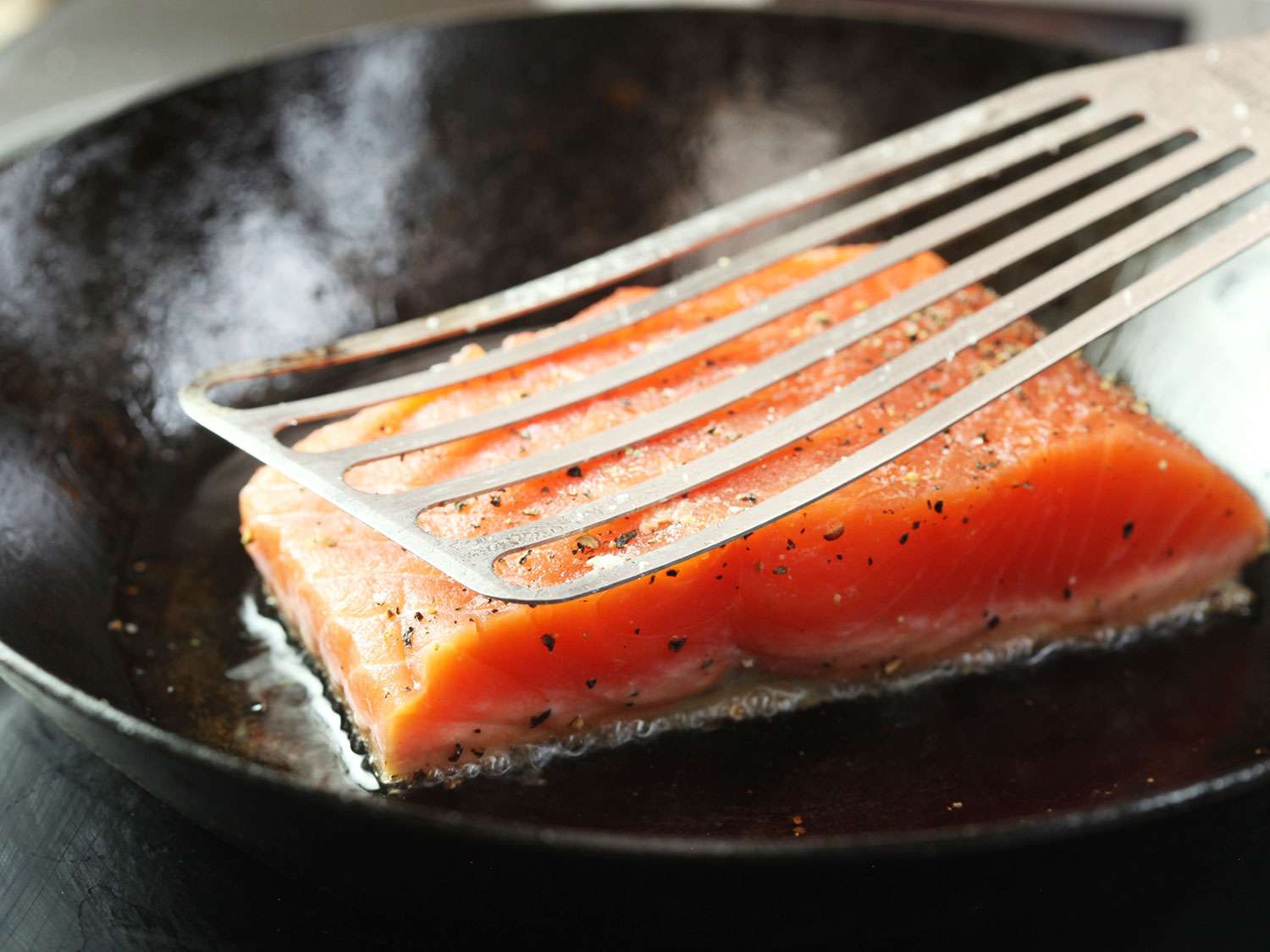 在热的碳钢煎锅中，用鱼刮刀压在植物油中烤好的三文鱼肉片上。