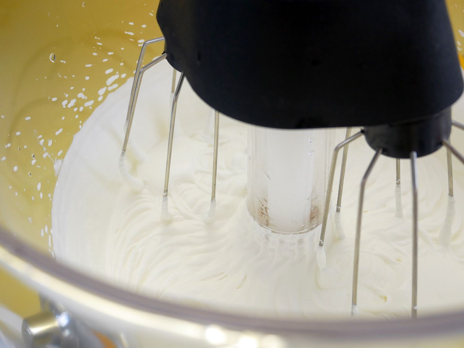 塑料碗中鲜奶油的特写镜头，多管齐下的搅拌器。