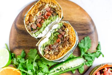 A Carne Asada burrito cut in half, exposing the rice, beans, steak, salsa and other fillings.
