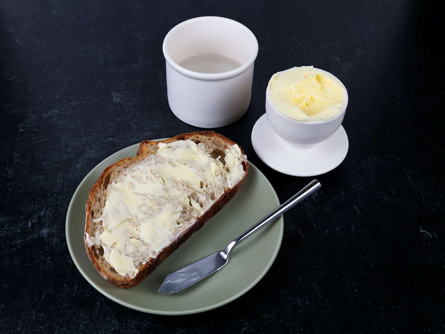 面包片上有一层厚厚的黄油，放在盘子里，旁边有一个黄油钟形陶罐