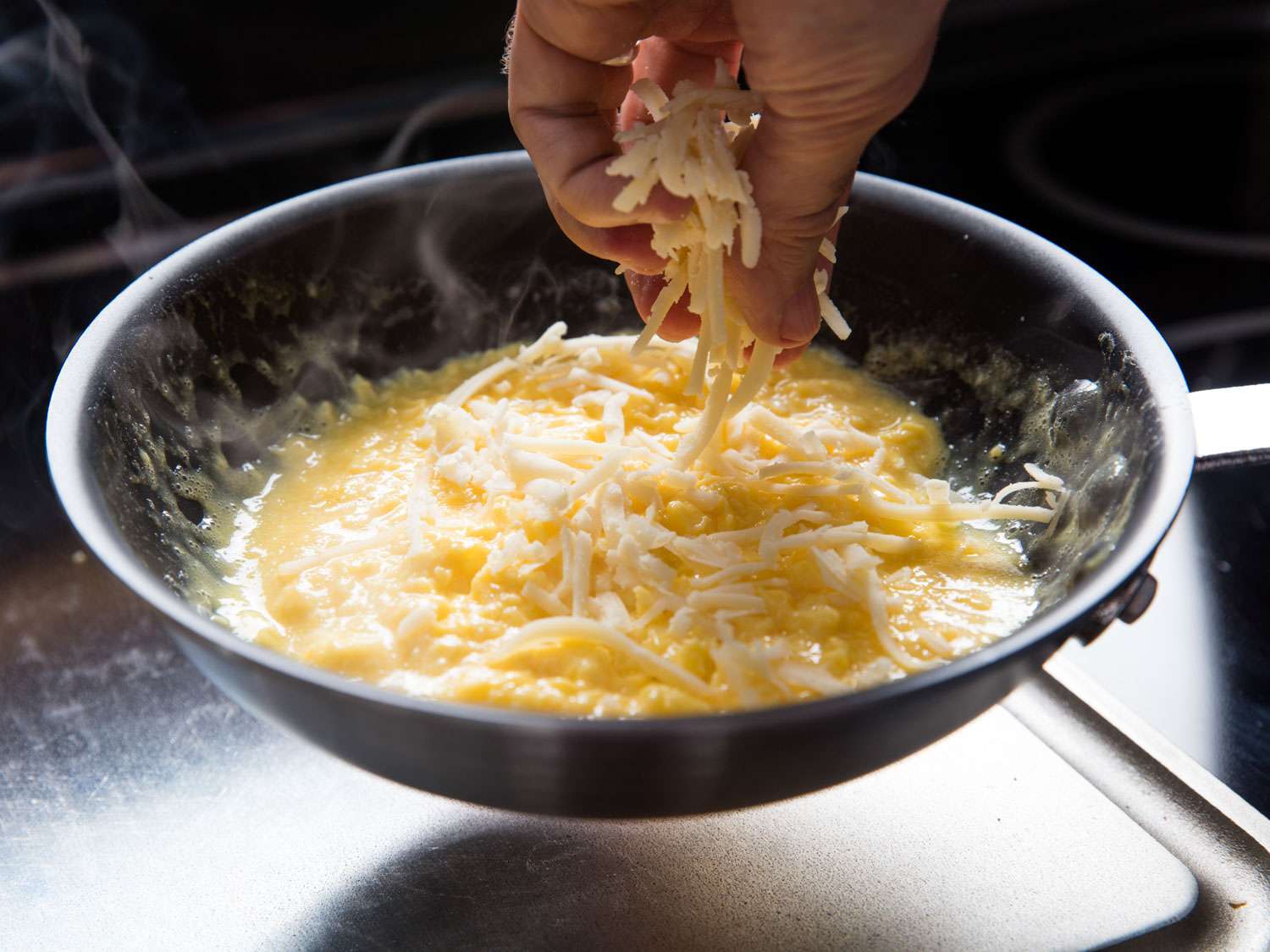 Sprinkling grated cheese into a pan of scrambling eggs
