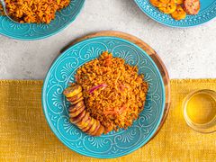 Overhead view of Jollof rice on a bright blue plate on top of a yellow table runner next to a glass of water