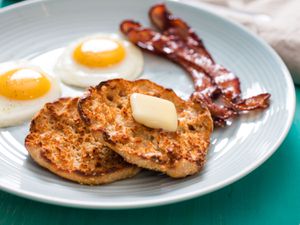 把自制的英式松饼撒上黄油，放在蓝色盘子上，旁边是两个单面鸡蛋和两片培根。