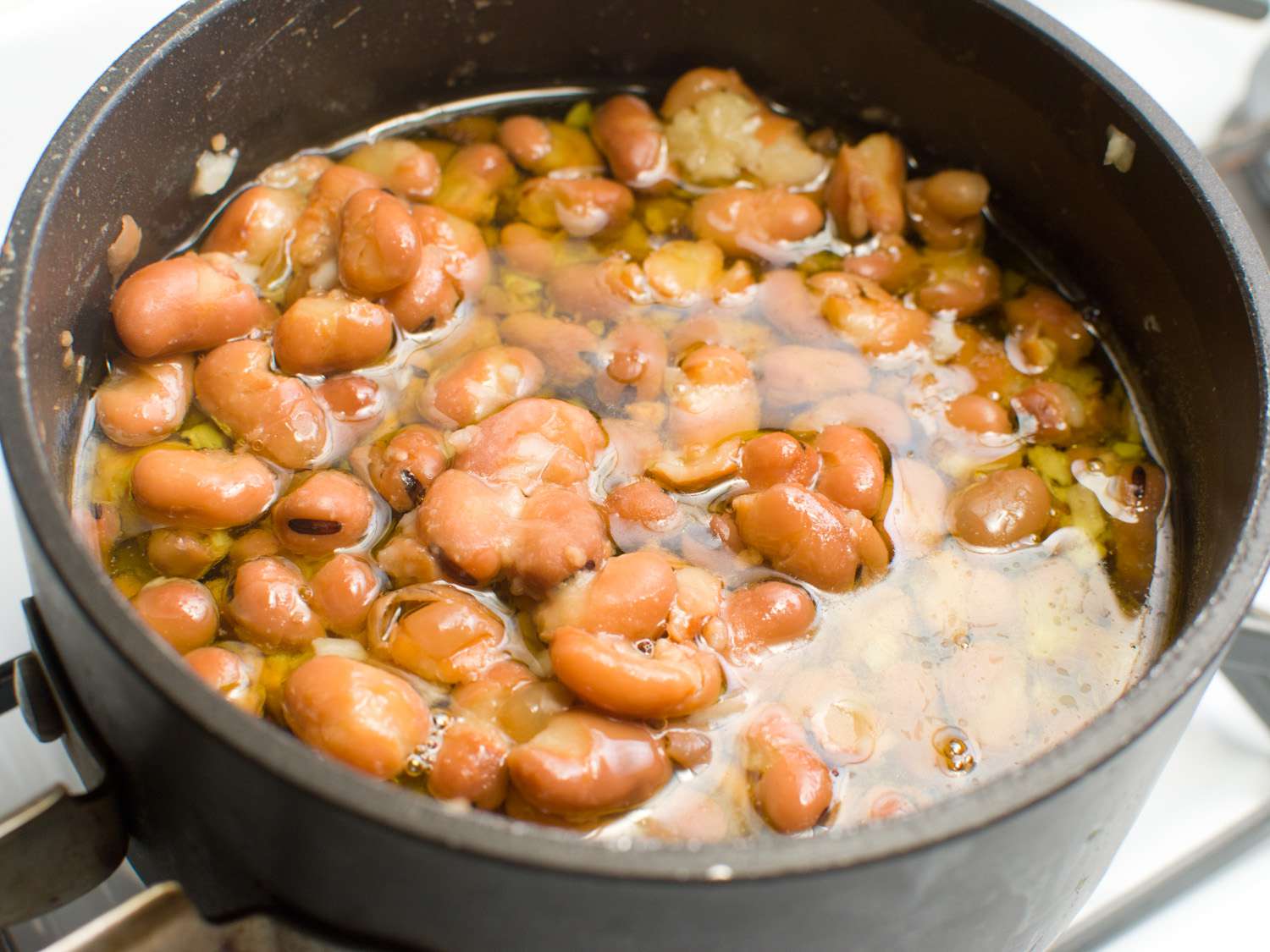 炖一锅蚕豆，将其部分浸入肉汤中，加入适量的橄榄油，准备炖煮。