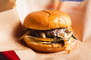 一个俄克拉荷马风格的洋葱汉堡，用熟食纸包装，装在红色的塑料熟食篮子里。