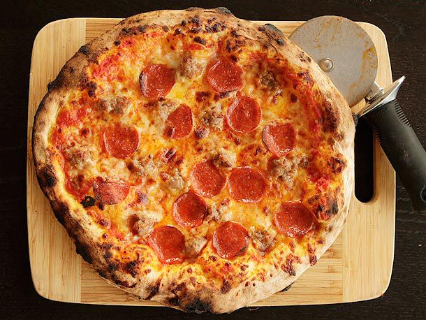 一个自制的纽约风格的意大利辣香肠披萨，放在带有披萨轮的切菜板上。gydF4y2Ba