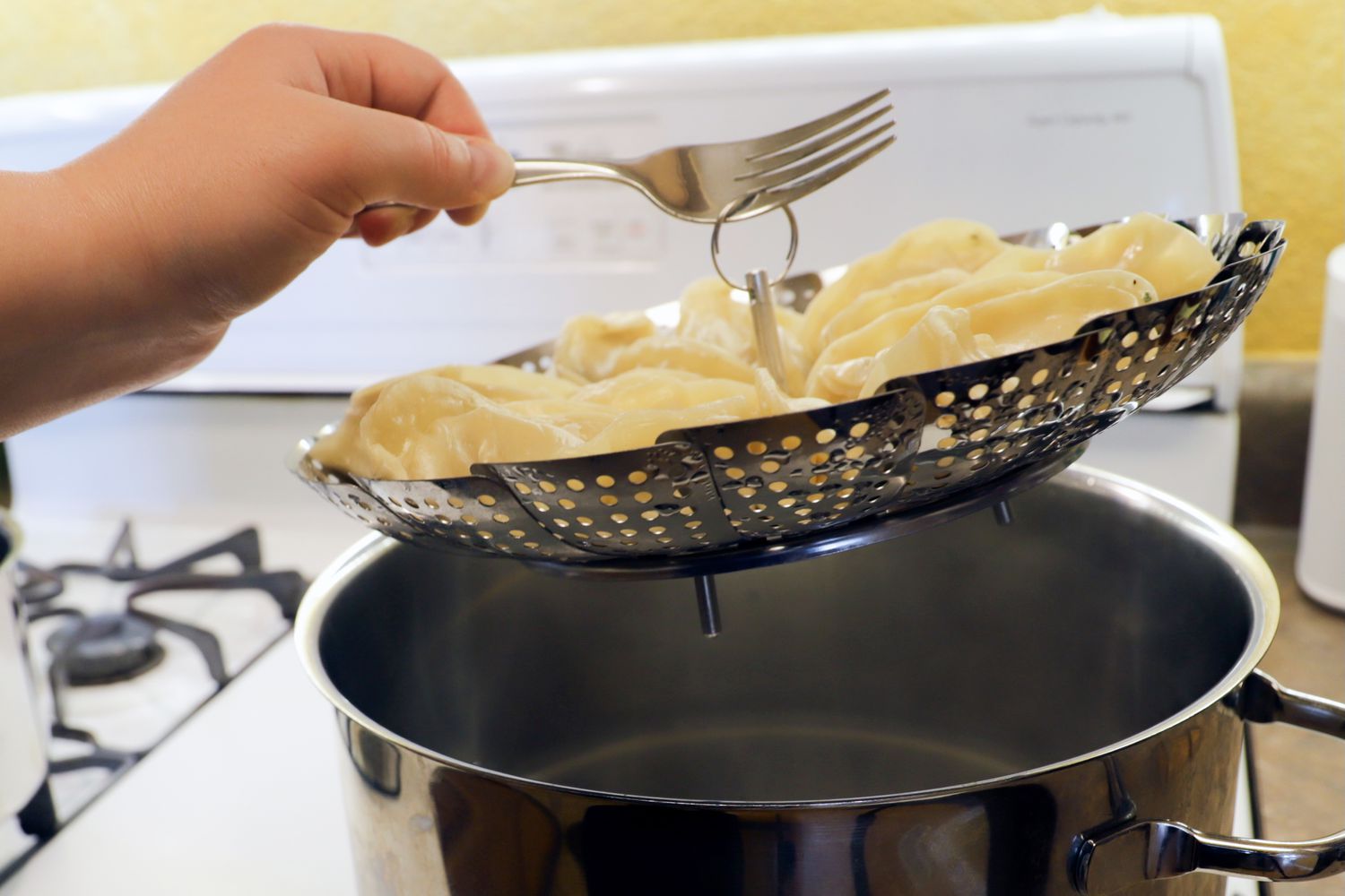 叉子从汤锅中提起装满饺子的蒸笼篮