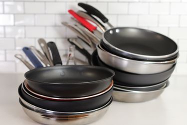 two stacks of various nonstick skillets against a white background