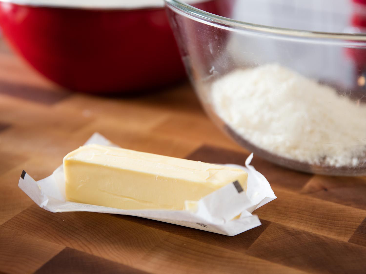 一块没有包装的黄油放在木板上。背景是一碗磨碎的帕尔马干酪。gydF4y2Ba