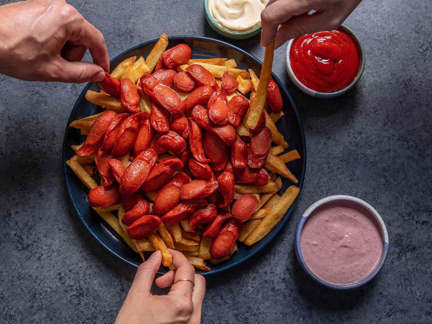 Hands grabbing French fries and hot dogs from a platter of salchipapas