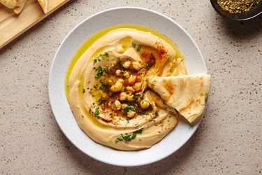 The best smooth hummus in a white round dish, with a piece of pita bread on the right hand side of the plate.