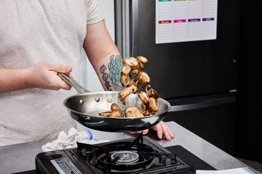 a person tossing mushrooms in a stainless steel skillet